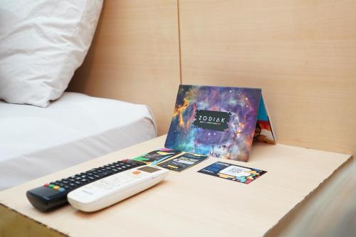 a table with a remote control and a book on a bed at Zodiak Paskal by KAGUM Hotels in Bandung