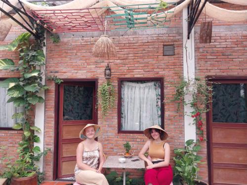 zwei Frauen auf einem Tisch vor einem Backsteingebäude in der Unterkunft Green Sunshine in Cần Thơ