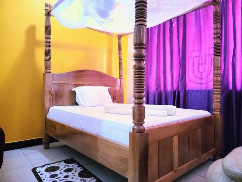 - une chambre avec un lit à baldaquin et des rideaux violets dans l'établissement Jm Lodge - Kunduchi, à Dar es Salaam