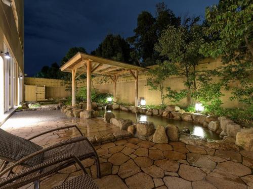 a stone patio with a pond and a pergola at ホテル京都エミナースManyonoyuHotelKyotoEminence in Kyoto