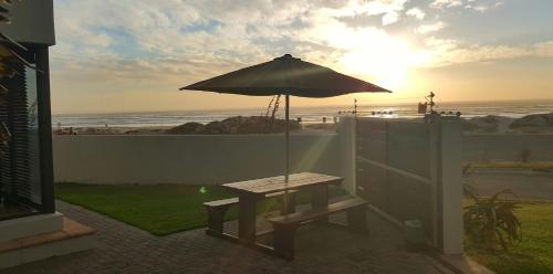 a picnic table with an umbrella in front of the beach at Beach Apartment Melkbosstrand in Melkbosstrand