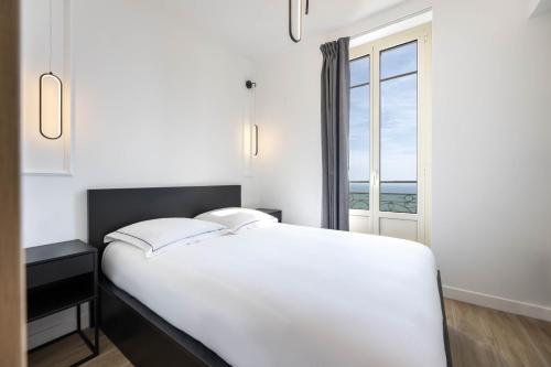 białe łóżko w pokoju z oknem w obiekcie MONACO SEA VIEW APARTMENTS w mieście Beausoleil