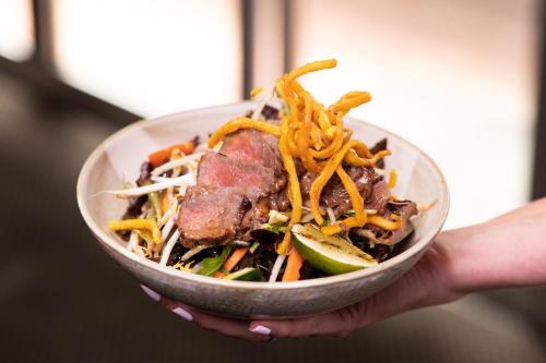 a person holding a bowl of food with meat and noodles at Family Hotel in Bathurst