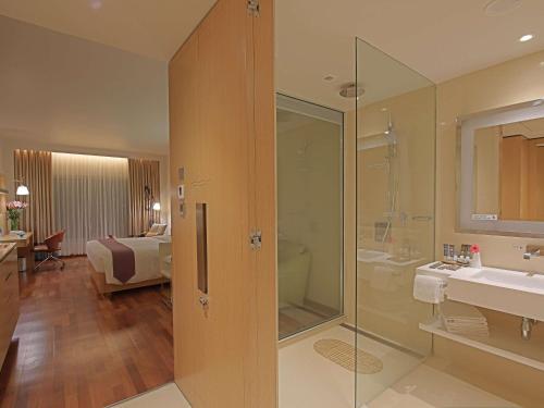 a bathroom with a shower and a sink and a bedroom at Novotel Visakhapatnam Varun Beach in Visakhapatnam