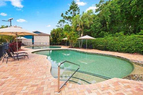 a swimming pool with umbrellas in a yard at Ocean View Apartment - Aqualuna Coffs Harbour in Sapphire Beach