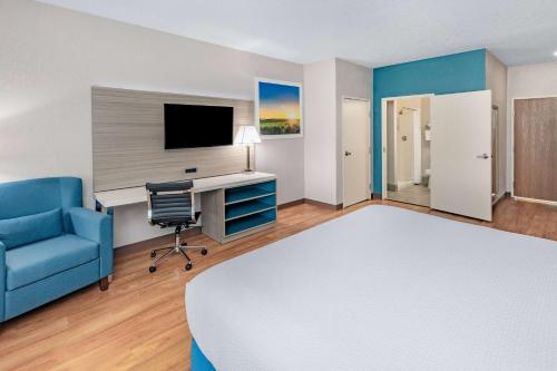 a hotel room with a bed and a desk and a blue chair at Days Inn & Suites by Wyndham San Antonio near Frost Bank Center in San Antonio