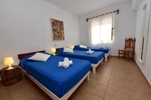 um quarto com quatro camas com lençóis azuis e uma janela em Costamar 13 em Es Pujols
