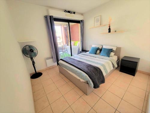 a bedroom with a bed with blue pillows and a fan at Le Dory - Appartement Centre Ville avec Terrasse, Parking & Wifi in Montpellier