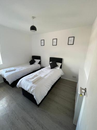two beds in a room with white walls and wood floors at Monochrome Emerald in Brentwood