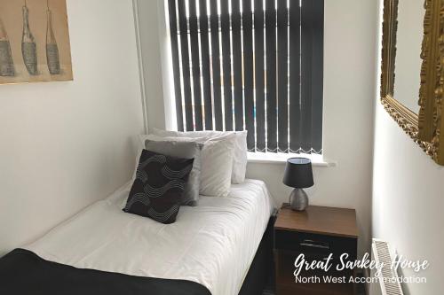 uma cama com lençóis brancos e almofadas ao lado de uma janela em Great Sankey Serviced Accommodation em Warrington