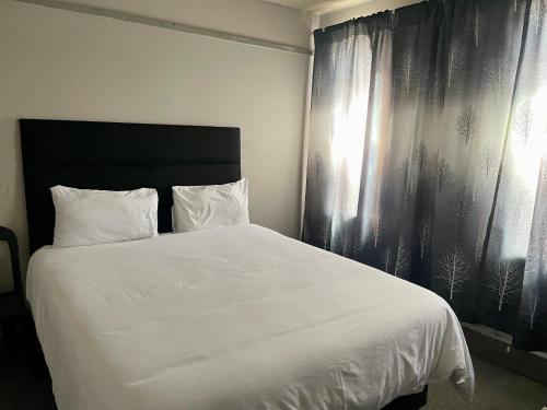 a bedroom with a large white bed and curtains at Stay Inn Lodge Randfontein in Randfontein