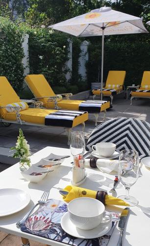 a table with chairs and plates and an umbrella at Fleur du Soleil Luxury Guesthouse in Franschhoek