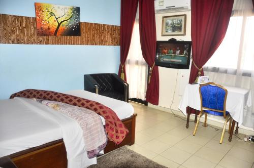 HOTEL DE LA VALLEE NEW في ياوندي: غرفة نوم بسرير وطاولة وتلفزيون