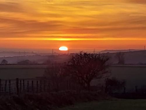 a sunset over a field with the sun in the sky at Converted rural stone cottage, Swansea in Swansea