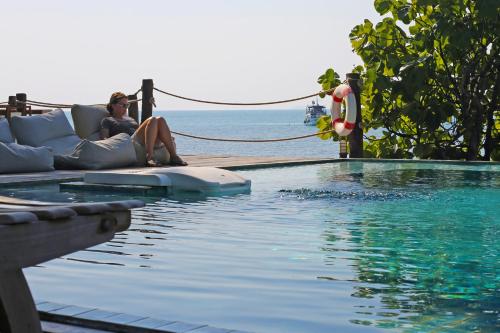 a woman sitting on a couch next to a swimming pool at Koh Munnork Private Island in Ko Munnork