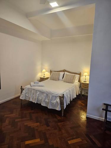 um quarto com uma cama com lençóis brancos e pisos em madeira em Obelisco Apartment em Buenos Aires