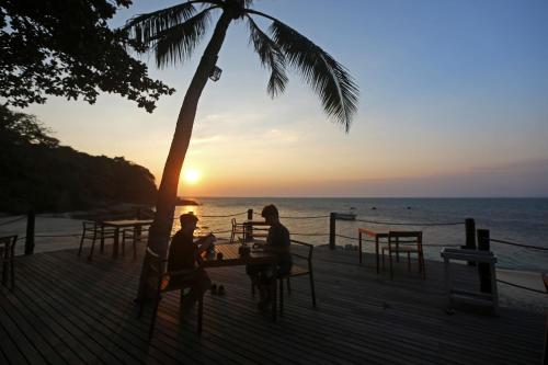 two people sitting at a table under a palm tree on the beach at Koh Munnork Private Island in Ko Munnork