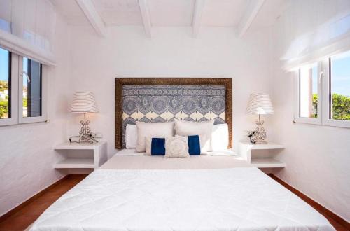 een witte slaapkamer met een groot bed met 2 lampen bij Villa Bini Sek in Binibeca