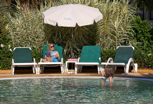 a woman sitting in chairs in a swimming pool at Hotel Porto Mare - PortoBay in Funchal