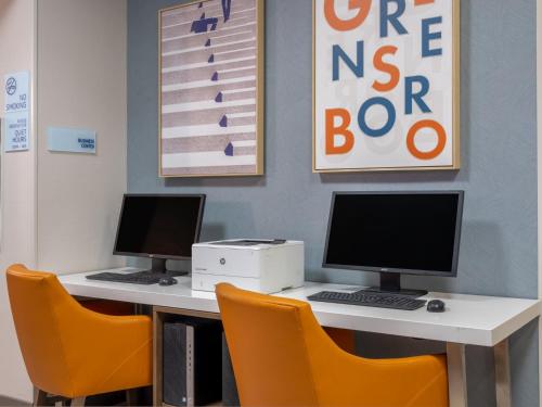 two computers sitting on a desk with orange chairs at Holiday Inn Express & Suites Greensboro - I-40 atWendover by IHG in Greensboro
