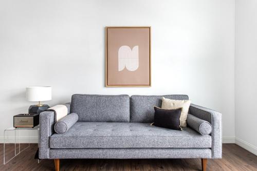 a grey couch in a living room with a picture on the wall at 1BR w Gym WD Steps from Newtonville Train BOS-353 in Newton