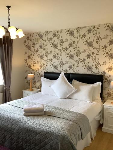 um quarto com uma cama com almofadas brancas e papel de parede floral em O' Sullivan's B & B em Killarney