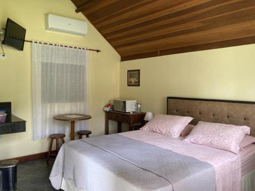 a bedroom with a bed and a table and a window at Pousada Colar de Ouro Chalés in Cunha