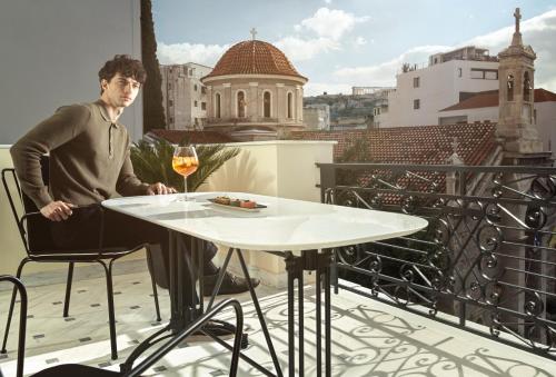 um homem sentado numa mesa numa varanda com um copo de vinho em Monument em Atenas