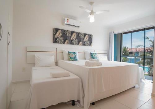 a white bedroom with a large bed and a window at DUPLEX 2 SUÍTES MONT SIÃO in Porto Seguro