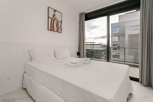 ein weißes Bett in einem Zimmer mit einem großen Fenster in der Unterkunft Rooftop | Piscina | Varanda #JA23 in Florianópolis