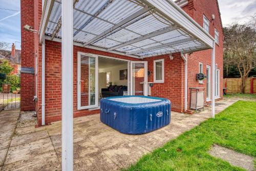 a covered patio with a blue ottoman in front of a brick house at Safari Stays - Gated - Sleeps 14 - Hot tub - Garden in Kidderminster