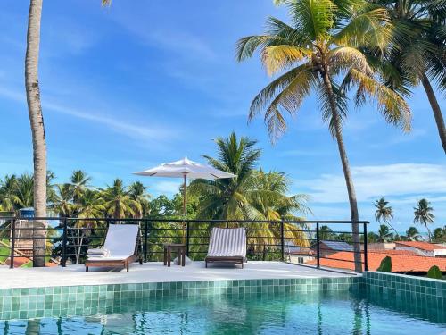 een zwembad met 2 stoelen en een parasol en palmbomen bij Milie Lounge Pousada in Japaratinga