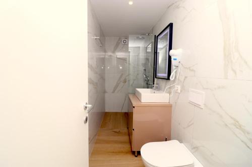 a white bathroom with a toilet and a sink at Fegi Rooms in Himare