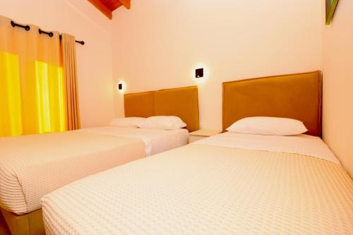 two beds in a room with white walls and yellow curtains at Fegi Rooms in Himare
