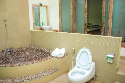 a bathroom with a toilet and a tub with a mirror at Araminth Guest House and Spa in Lovina