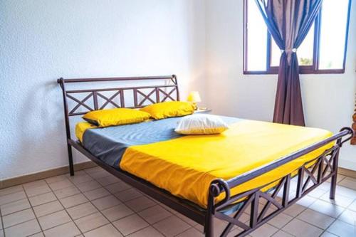 um quarto com uma cama com lençóis amarelos e uma janela em Bel appartement T2 * Netflix * Terrasse* Parking em Kourou