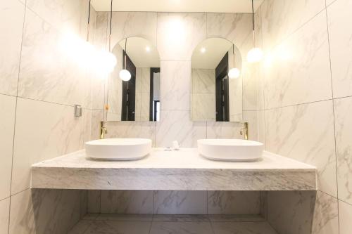 two sinks in a bathroom with two mirrors at Sokcho Business Hotel CAMEL in Sokcho