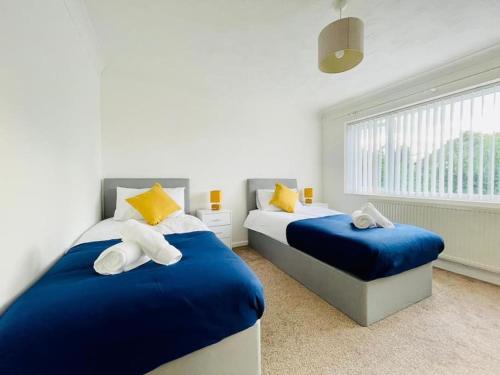 a bedroom with two beds with blue sheets and yellow pillows at Spacious 5 Bedroom house with free parking by Hostaguest in Luton