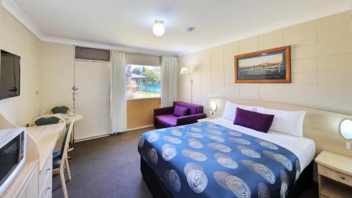 Habitación de hotel con cama y silla morada en Cootamundra Gardens Motel, en Cootamundra