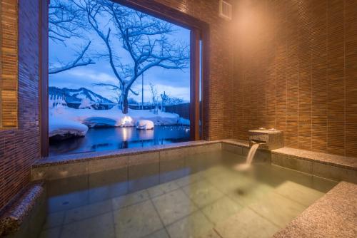 a bathroom with a bath tub with a large window at Onogawa Onsen Kajikaso in Yonezawa