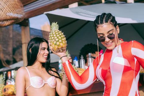 two women in bathing suits holding a pineapple at SUNSET BEACH in Playa Blanca