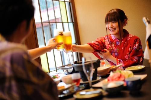a woman holding up two glasses of beer at a table at Onogawa Onsen Kajikaso in Yonezawa