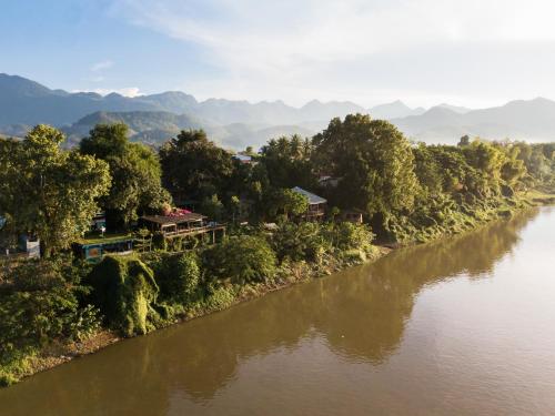 a river with houses and trees and mountains in the background at Ock Pop Tok Mekong Villa in Luang Prabang