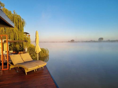 a deck with a chair and an umbrella on the water at Ark-imedes - Unique float home on the Murray River in White Sands