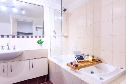 a bathroom with a sink and a tub with a laptop on a tray at Peppi Lane Stay in Margaret River Town