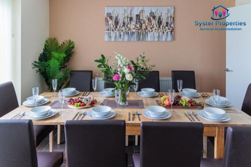 een houten tafel met stoelen en een grote tafel met bloemen bij Quiet & Comfortable Leicester Stay, Glen View, Free Parking in Leicester