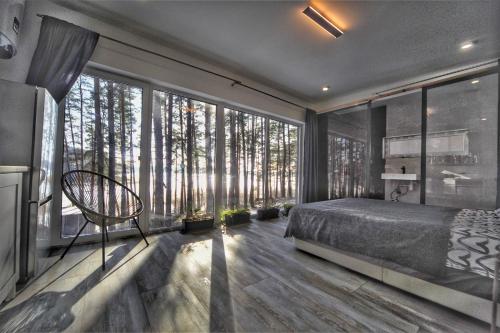 a bedroom with a bed and large windows with trees at GaujaClub - our BOSE and Bang&Olufsen lofts on a lake in Gauja