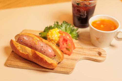 a hot dog on a bun with tomatoes and a cup of soup at BEB5 Tsuchiura by Hoshino Resorts in Tsuchiura