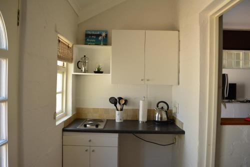 a kitchen with white cabinets and a black counter top at Pelican Cottage - 800m from Beach & Yacht School in Hout Bay