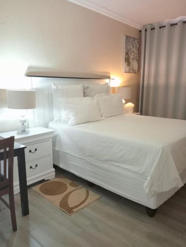 1 dormitorio con 1 cama blanca grande y escritorio en KnB Guesthouse, en Rustenburg